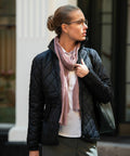 A person with glasses and hair tied back is wearing a Nimbus NB98F quilted black jacket, white shirt, and a light pink scarf while standing outdoors.