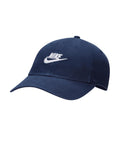 The Caps is a navy blue baseball cap with a curved peak, white embroidered Nike logo and swoosh on the front, ventilation eyelets, and a top button.