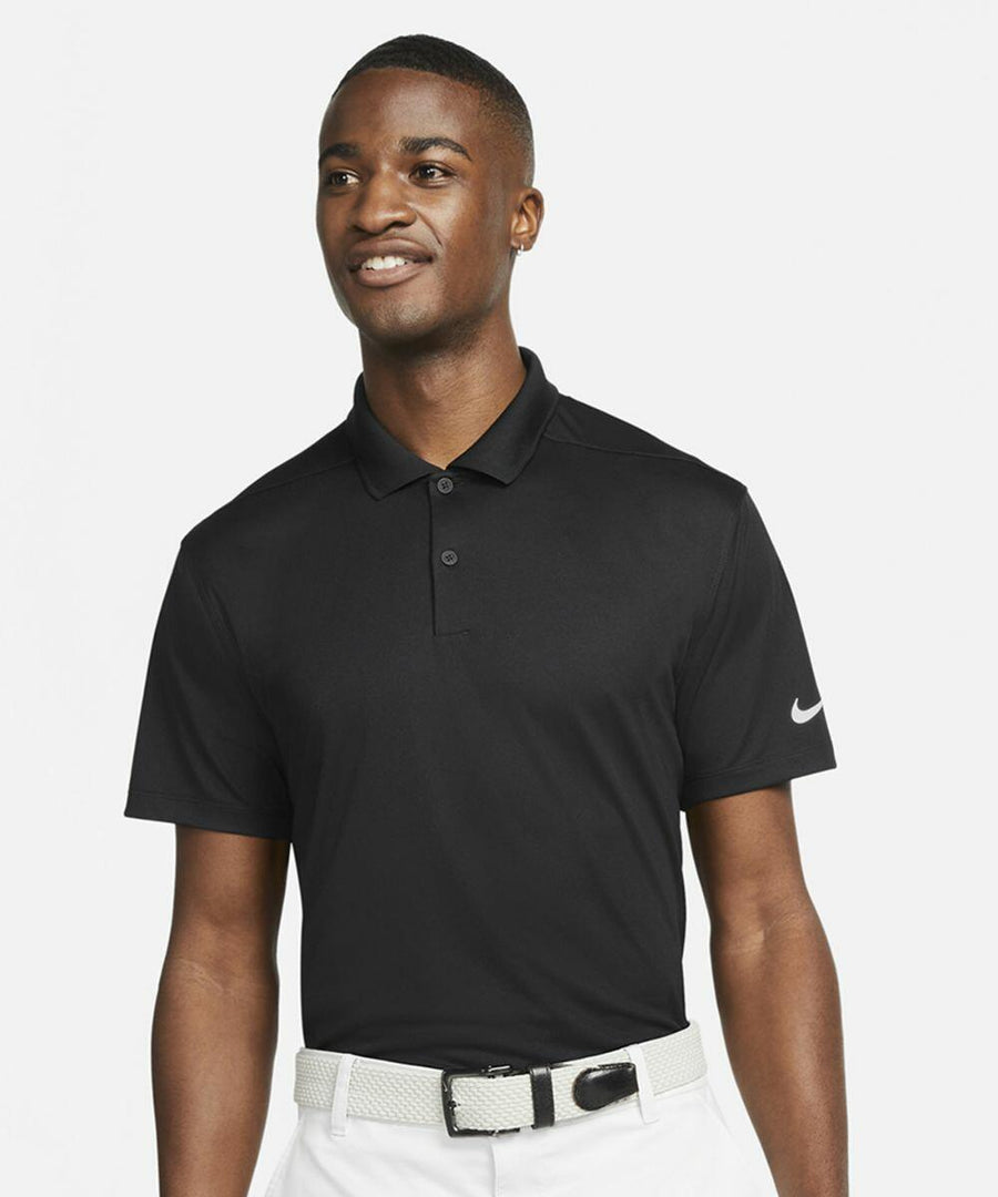 A person wearing a black Nike NK342 polo shirt and white belt smiles, standing against a plain white background.