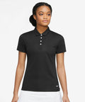 A woman wearing a black short-sleeve polo shirt with a small Nike NK344 logo on the lower left, standing against a plain white background.