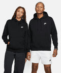 Two individuals stand side-by-side, both wearing black Nike NK387 hoodies. The person on the left wears dark pants, and the person on the right wears white shorts.