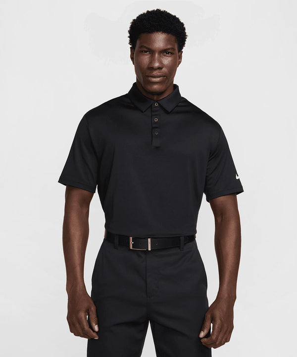 A man stands facing forward, wearing a black Nike Dri-FIT Tour solid polo with a three-button placket and black trousers. His expression is neutral and his arms are relaxed at his sides.
