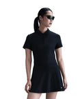 A person wearing black sunglasses, a black Nike Women's Dri-FIT Victory short sleeve polo, and a black skirt stands against a white background with their hair tied in a low ponytail.