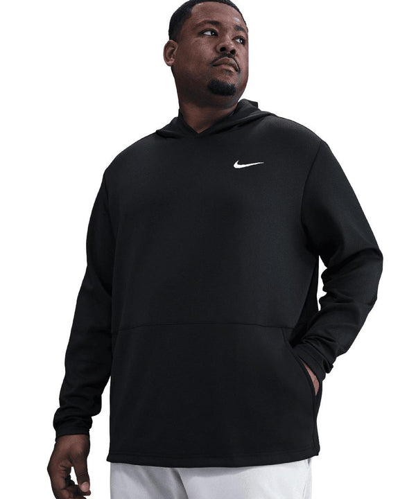 A man stands with one hand in his pocket, looking left, wearing a black Nike Dri-FIT Victory Therma Flex hoodie with a white logo on the left chest and light-coloured trousers. The background is plain white.