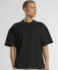 A person with short hair wears the Heavy Jersey oversized tee by New Morning Studios in black, standing against a plain light background and looking to the left.