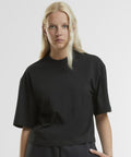 A woman with long, straight blonde hair wears the Women's oversized tee by New Morning Studios in black. She stands against a light background, looking directly at the camera with a neutral expression.