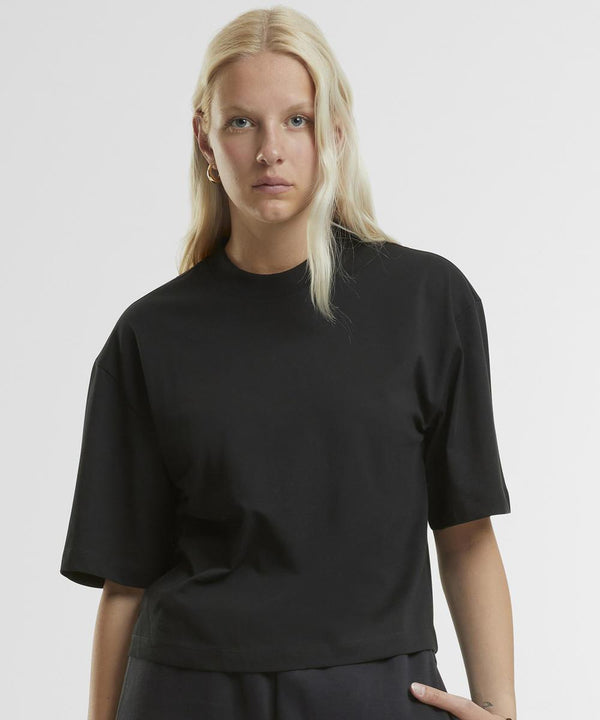 A woman with long, straight blonde hair wears the Women's oversized tee by New Morning Studios in black. She stands against a light background, looking directly at the camera with a neutral expression.