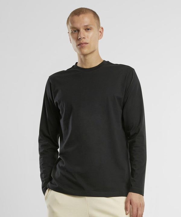 A person wearing a regular fit long-sleeve shirt by New Morning Studios in black with light-coloured trousers stands against a plain white background, looking at the camera with a neutral expression.