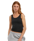 A woman with long, straight reddish-brown hair wears the New Morning Studios women's basic vest in black and light grey sweatpants, standing against a plain white background.