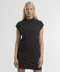 A person with long blonde hair stands against a white background wearing the Women's extended shoulder dress by New Morning Studios, a short-sleeved, black, knee-length outfit. They face the camera with a neutral expression.