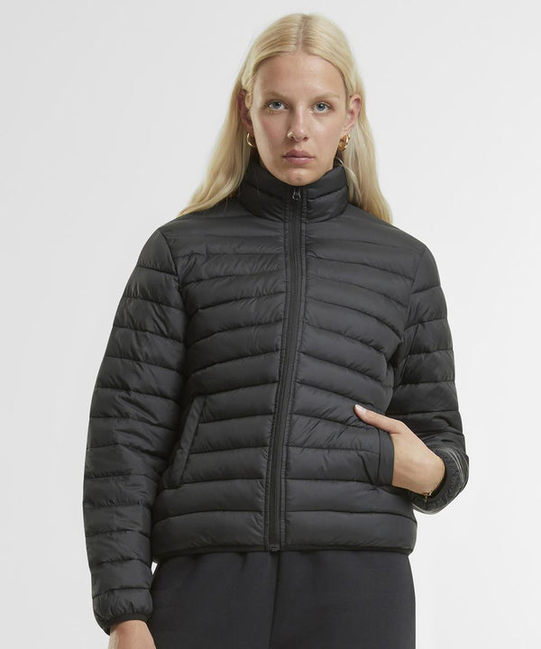 A woman with long blonde hair wears the New Morning Studios women's light puffer jacket in black, featuring horizontal quilting and a zip-up front, standing against a plain white background with one hand in her pocket.