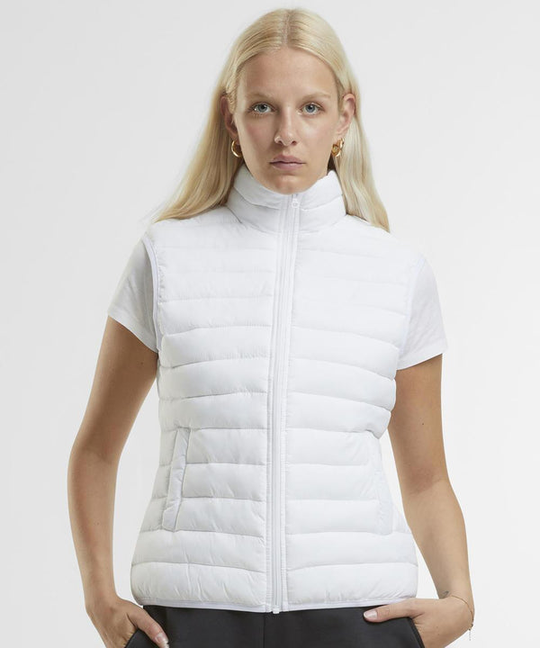 A woman with long blonde hair models the New Morning Studios Women's light puffer gilet over a white short-sleeve shirt, standing against a plain white background and looking straight at the camera.