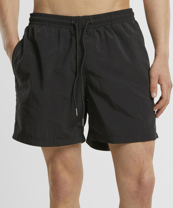 A person wearing New Morning Studios' Basic swim shorts with an elasticated waistband and relaxed fit, hands in pockets, stands against a plain background.