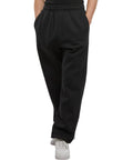 A person models the Basic track bottoms by New Morning Studios, paired with white trainers. The photo shows only the lower half of the body, hands in pockets, set against a plain background.