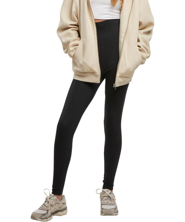 A person wears women's cotton leggings by New Morning Studios, paired with a beige zip-up jacket, white crop top, and grey trainers. Their hands are in the jacket pockets and their face is not shown.