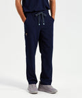 A person wearing navy blue NN500 scrub pants by Onna with hands in pockets and gray sneakers stands against a plain background.