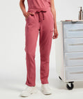 A person wearing Onna NN600 pink scrub pants with a drawstring, standing beside a rolling cart with drawers.