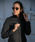 A woman wearing sunglasses and a dark quilted jacket stands outdoors, partially zipping up her Nimbus NP11F jacket.
