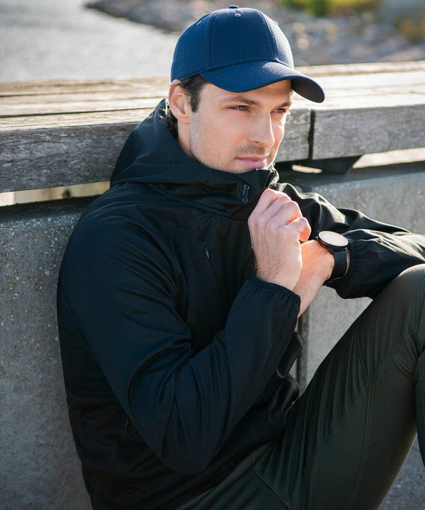 A man wearing a dark jacket and blue cap is sitting outdoors, looking into the distance, and adjusting the collar of his Nimbus NP14M jacket.