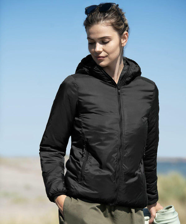 A woman in a black zip-up jacket stands outdoors, holding a Nimbus NP16F in her left hand. She has sunglasses atop her head and the background features a blue sky and blurred landscape.