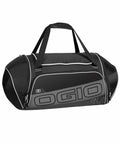 A black OGIO OG021 gym duffel bag with white piping, featuring a large central compartment, two side pockets, and carrying handles.