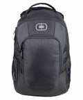 A black and grey OG036 backpack from Ogio with multiple zipped compartments and a carrying handle at the top. The backpack has a logo with an interlocking "O" design on the front.