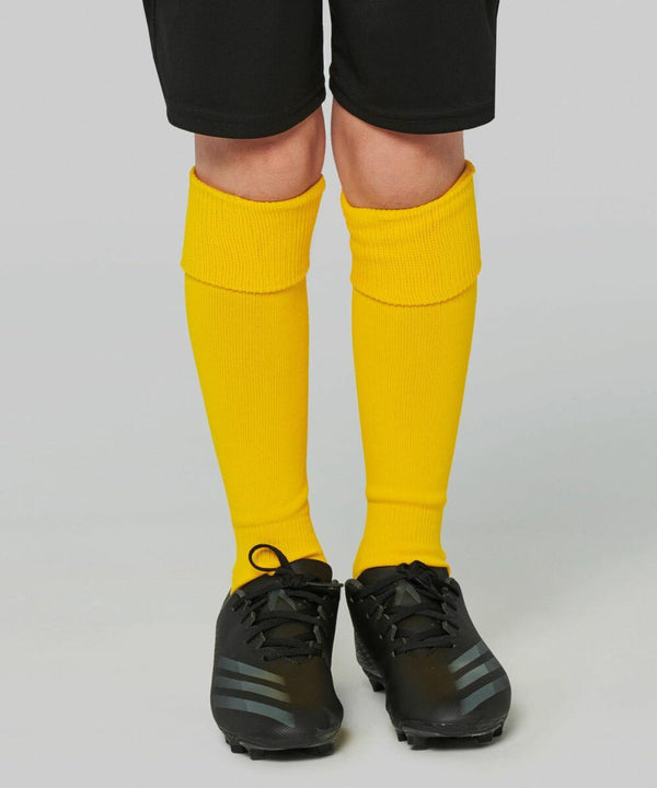 A pair of legs wearing yellow Kariban Proact PA016 soccer socks and black soccer cleats, with black shorts visible at the top.