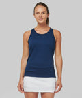 A person stands against a gray background wearing a navy blue sleeveless top and a white skirt, looking straight at the camera, showcasing the PA442 by Kariban Proact.