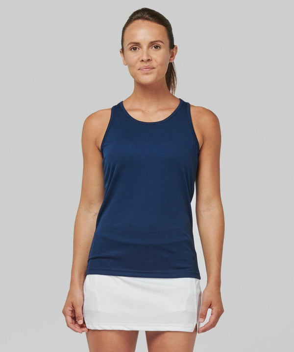 A person stands against a gray background wearing a navy blue sleeveless top and a white skirt, looking straight at the camera, showcasing the PA442 by Kariban Proact.