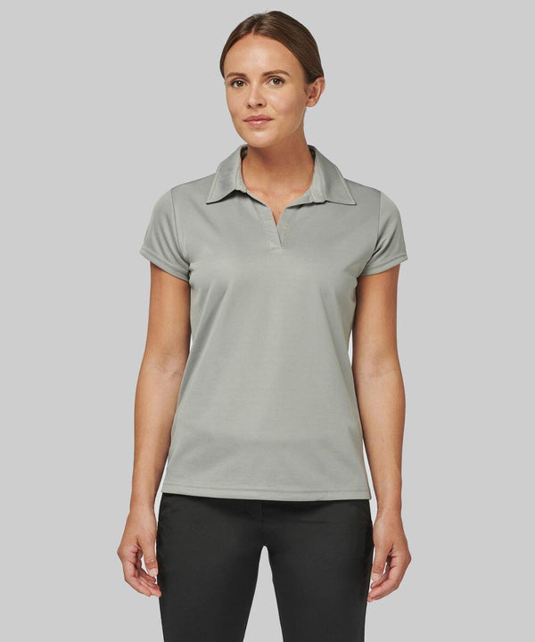 A person stands facing forward, wearing a light grey Kariban Proact PA483 polo shirt and black pants against a plain grey background.