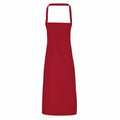 A Premier PR102 apron, featuring a classic design with a neck loop and waist ties, is displayed against a white background. This apron comes in red.