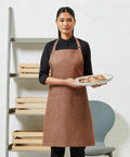 A woman wearing a brown apron and black shirt holds a plate of Premier PR113 while standing in front of an empty shelving unit and a grey chair.