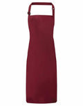 The Premier PR115 is a simple red apron featuring a neck strap and waist ties, displayed against a white background.