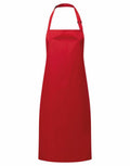 The PR115 by Premier is a vibrant red apron featuring a simple, classic design with a neck strap and knee-length cut. It boasts a smooth texture without any visible patterns or pockets.