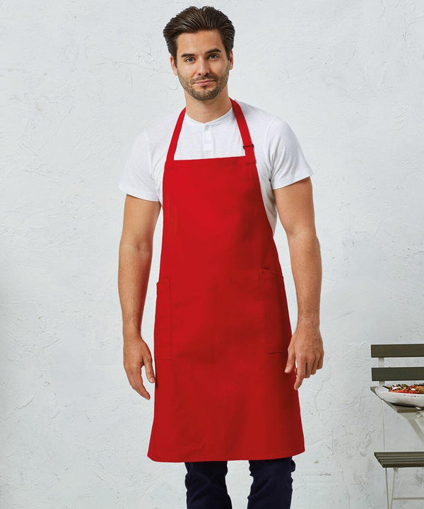 A man in a red apron stands with his hands in his pockets against a plain white background. He is wearing a white t-shirt and dark pants. There is part of a small table visible on the right, showcasing the Premier PR120.