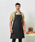 A man stands wearing a beige shirt and a dark apron in front of a light textured background. A table with Premier PR126 and a jar is visible beside him.