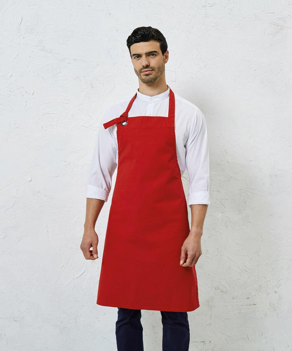 A man wearing a Premier PR130 white shirt and a red apron stands against a white textured background.