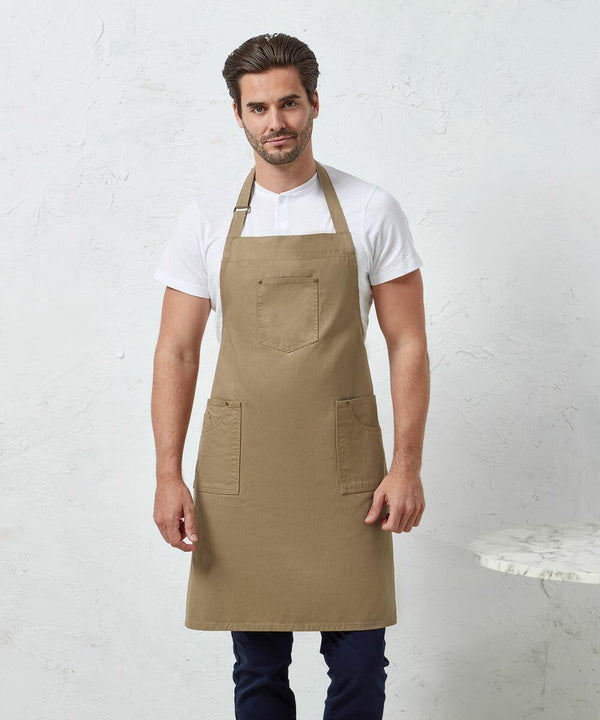 A man wearing a white t-shirt and a brown apron stands in front of a white textured wall. There is a small round marble table, the Premier PR132, on the right side of the image.
