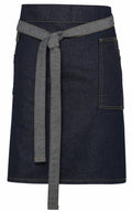 The PR135 by Premier is a dark denim apron featuring a front pocket and long, adjustable tie straps. It showcases visible yellow stitching, and the hem falls above the knees.