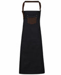 A Premier PR136 apron in black, featuring a brown adjustable neck strap and a small front pocket.