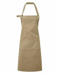 The Premier PR137 is a tan kitchen apron featuring an adjustable neck strap and two spacious front pockets.