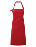 The Premier branded PR137 apron, in red, features a neck strap, a front pocket, and a metal grommet on the top left side. It is displayed against a white background.