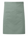 A waist apron in a shade of green, featuring a large front pocket and crafted from smooth fabric, is presented on a plain white background. The apron is labeled as Product Name: PR141 by the brand Premier.