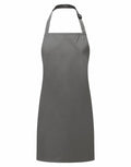 The PR145 apron from Premier is a solid gray design featuring a neck strap and waist ties, presented against a white background. The apron showcases a minimalistic look without any patterns or pockets.