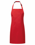 Introducing the PR145 apron by Premier: This vibrant red apron features a neck strap with an adjustable buckle. Its simple and clean design extends to a point, making it perfect for cooking or crafting activities. Crafted from smooth, durable material, this apron combines style with functionality.