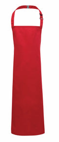 A vibrant red PR149 apron from Premier, featuring a neck strap and an adjustable buckle, set against a white background. The design is plain with no visible patterns or logos.