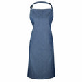 The PR150 by Premier is a minimalist blue denim apron featuring a neck loop and waist tie. It boasts a sleek design with no visible pockets or logos, offering a smooth texture that provides coverage from the chest to the knees.