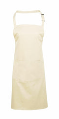 The Premier PR154 apron features a beige color with a large front pocket and an adjustable neck strap, showcased against a white background.