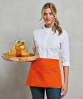 A person wearing a white shirt and orange apron is holding a wooden tray with a pitcher and glasses of orange beverage from Premier's PR155 collection.