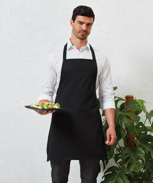 A man in a white shirt and black apron holds a plate of Premier PR165. A green plant is partially visible on his side.